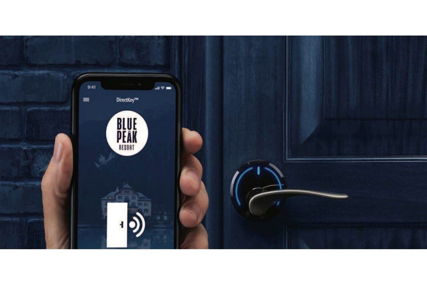 Hand holding smartphone with DirectKey app near a smart door lock.