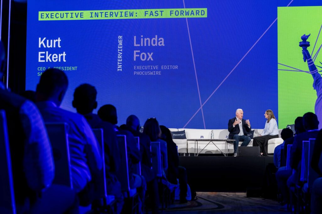 A speaker and interviewer on stage address attendees at The Phocuswright Conference